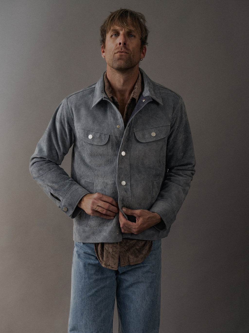 David Dangelo Caldwell grey suede trucker jacket with exposed seams and proprietary hardware, worn by a man with light wash jeans.