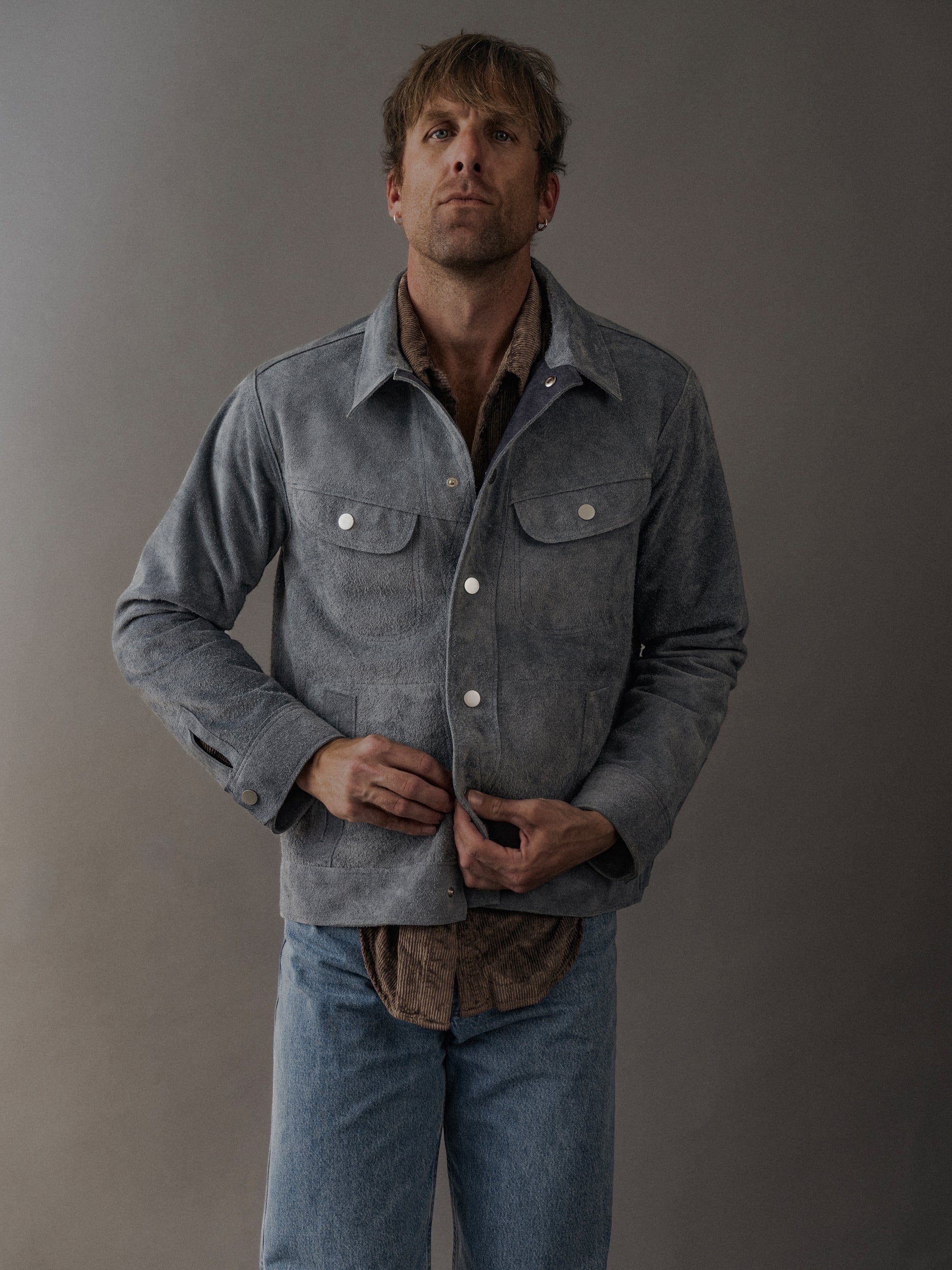 David Dangelo Caldwell grey suede trucker jacket with exposed seams and proprietary hardware, worn by a man with light wash jeans.
