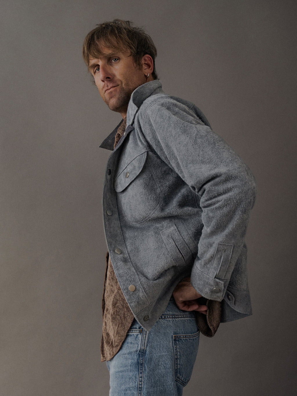 David Dangelo Caldwell grey suede trucker jacket with exposed seams and button closure, worn by a man with jeans.