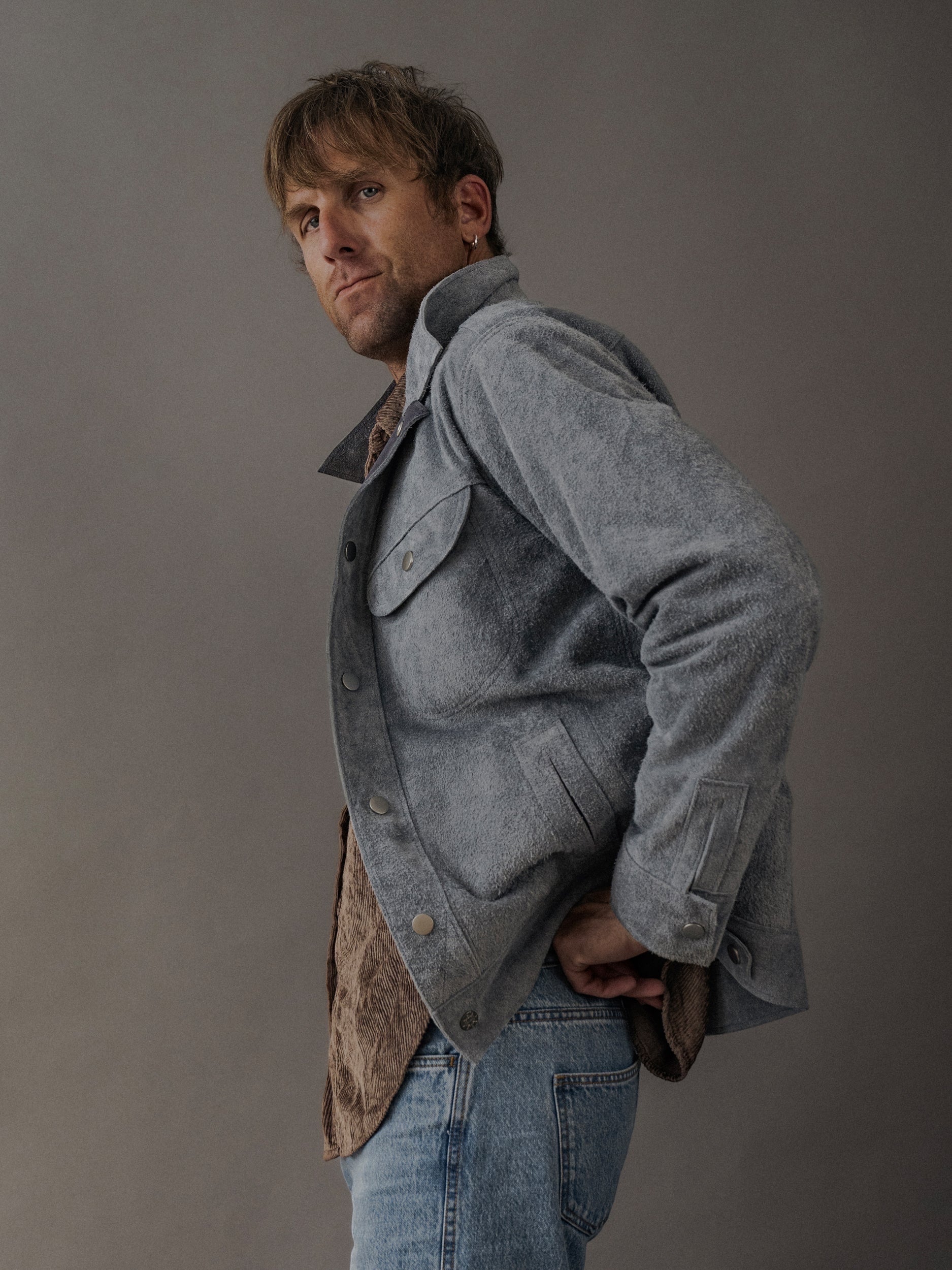 David Dangelo Caldwell grey suede trucker jacket with exposed seams and button closure, worn by a man with jeans.