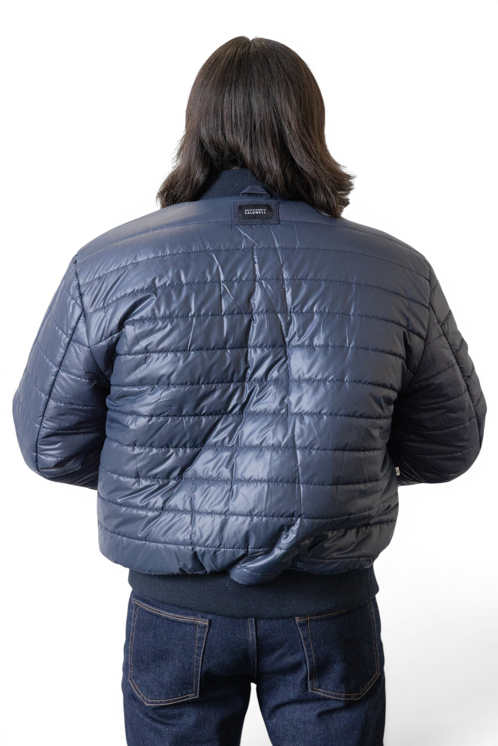 David Dangelo Caldwell navy blue puffer bomber jacket with quilted detailing and ribbed cuffs. Worn by a person with dark hair.