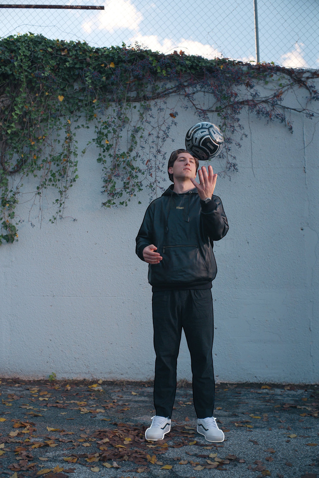 David Dangelo Caldwell black reversible lamb leather hoodie with oversized hood and zipper pockets, worn by a man juggling a soccer ball.