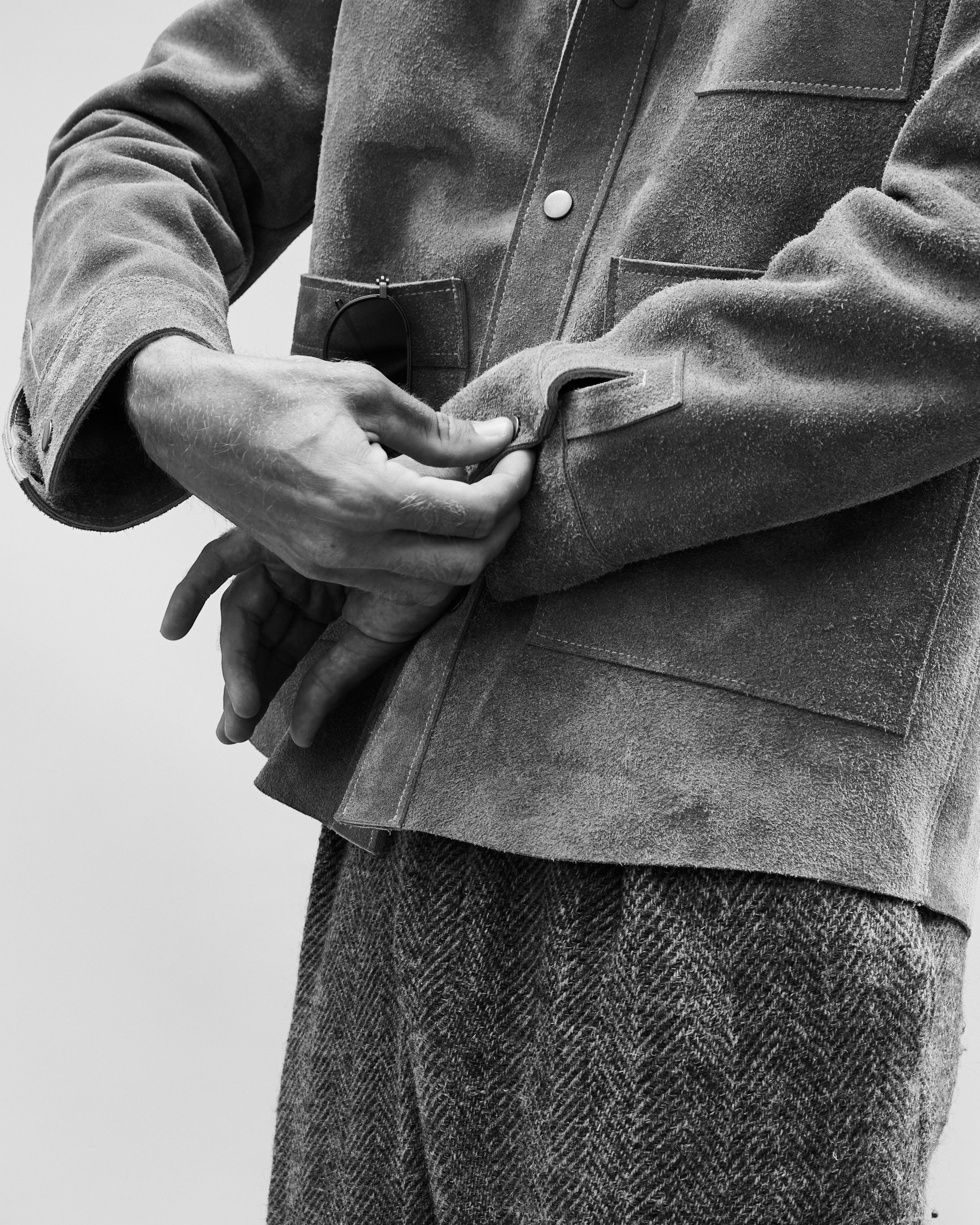 David Dangelo Caldwell grey suede jacket with two patch pockets and custom hardware, worn by a man adjusting the cuff.